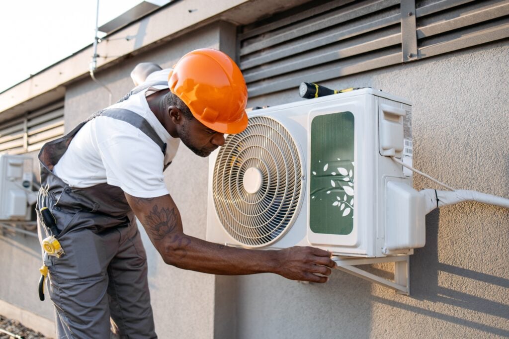 Male master fixing conditioner and checking fan outdoors