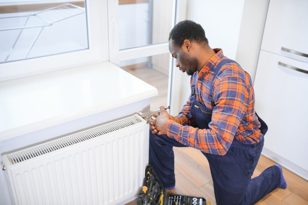 Man in workwear overalls using tools while installing or repairing heating radiator in room | Dan's HVAC