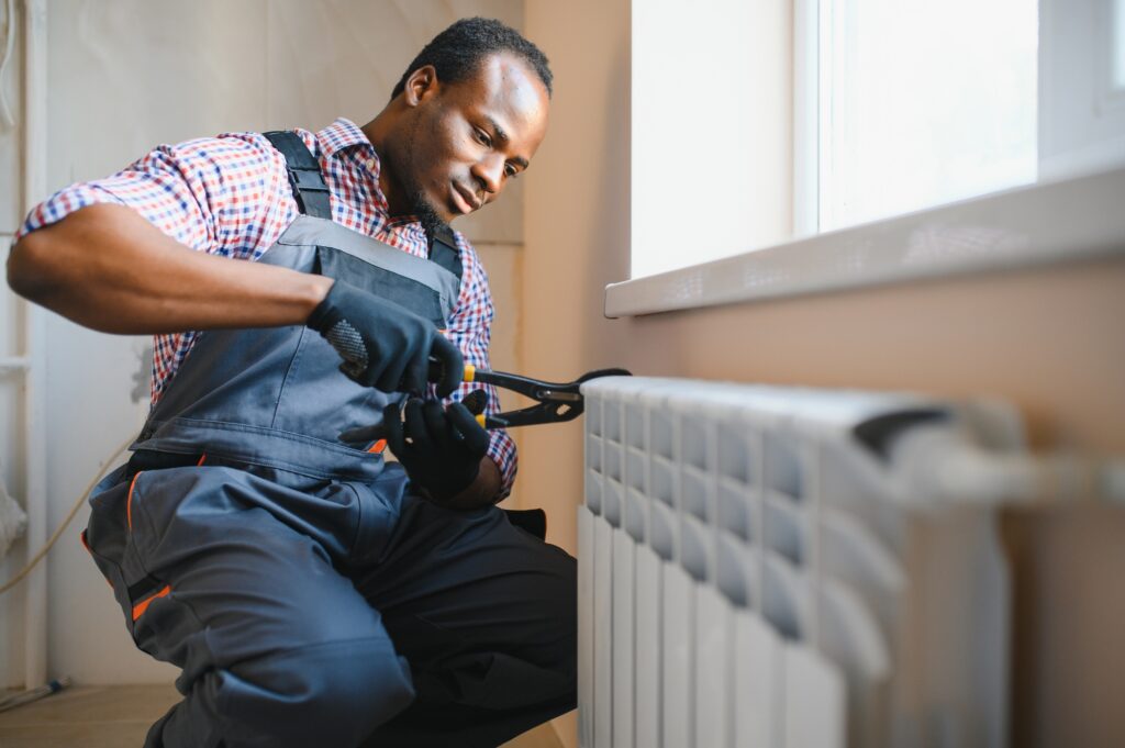 Man in workwear overalls using tools while installing or repairing heating radiator in room | Dan's HVAC