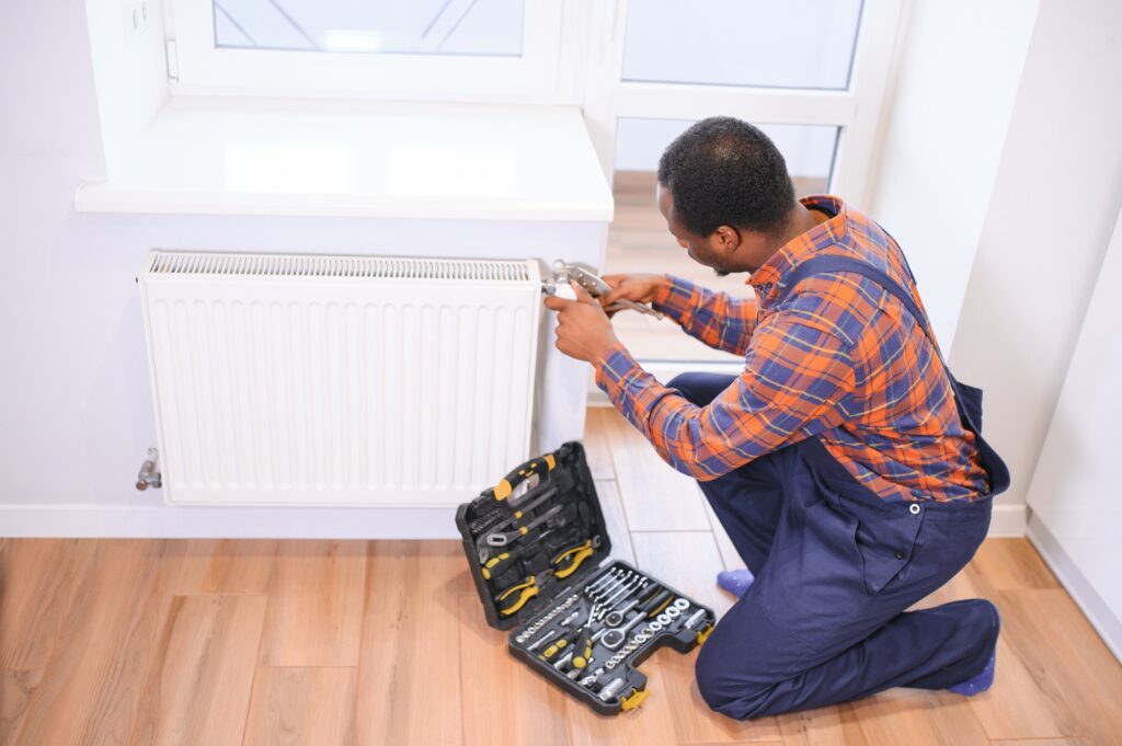 Man in workwear overalls using tools while installing or repairing heating radiator in room | Dan's HVAC