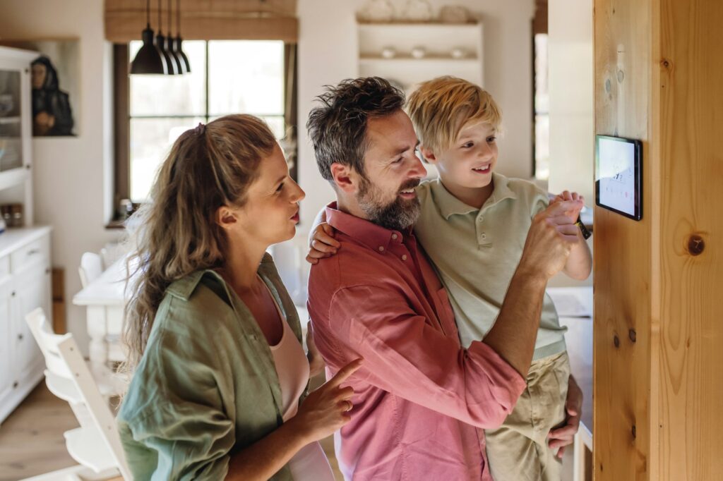 family looking at smart thermostat adjusting lowering heating temperature at home concept of 1024x682